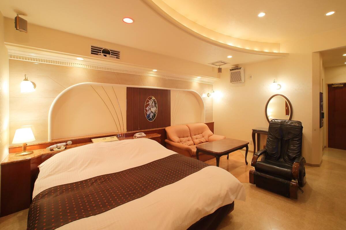 Una habitación de hotel con una cama grande, un sofá, una mesita, un sillón de cuero y un espejo.