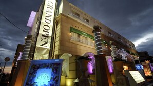 Un hotel con un vistoso cartello 'GRAND OPEN', un balcone con ringhiera e un grande cartellone illuminato.