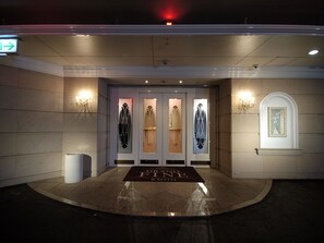 A hotel entrance with a grand foyer, a reception desk, and a wall-mounted painting.
