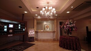 Una hall con una reception, un lampadario, un'esposizione floreale e un tappeto con la scritta 'GRAND HOTEL KYOTO'.