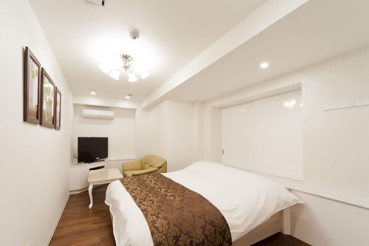 Una habitación de hotel con cama, escritorio con televisor, silla y armario.