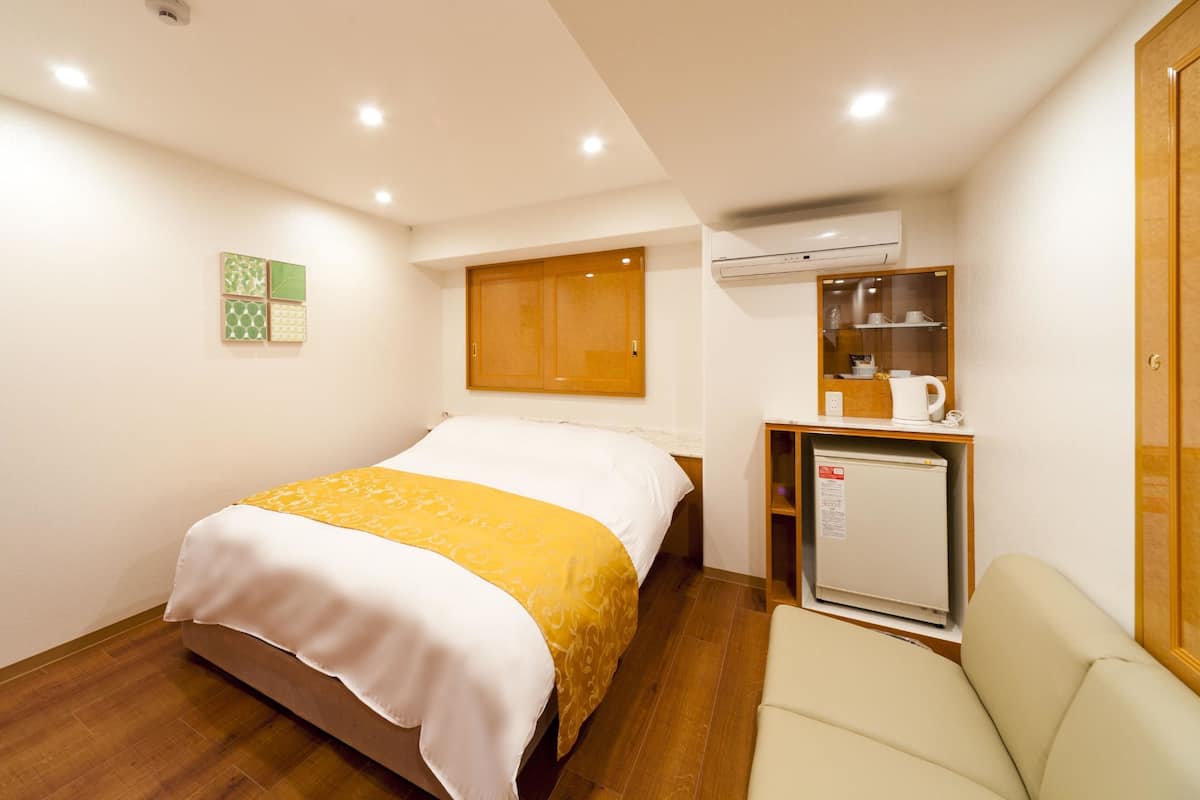 Una habitación de hotel con una cama, una kitchenette pequeña, una silla y un armario de madera.