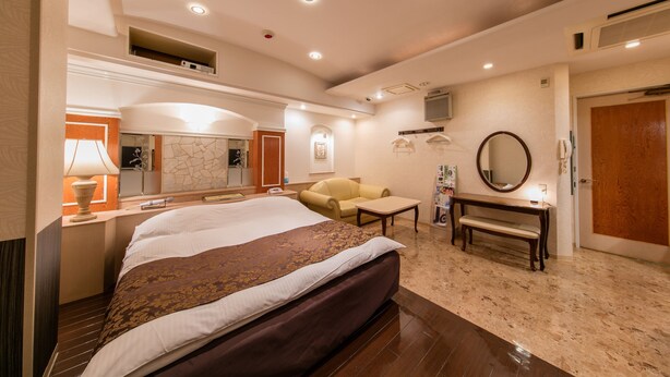 A hotel room with a large bed, a sofa, a small table, a mirror, and a door. - Fine Tsu (Tsu)