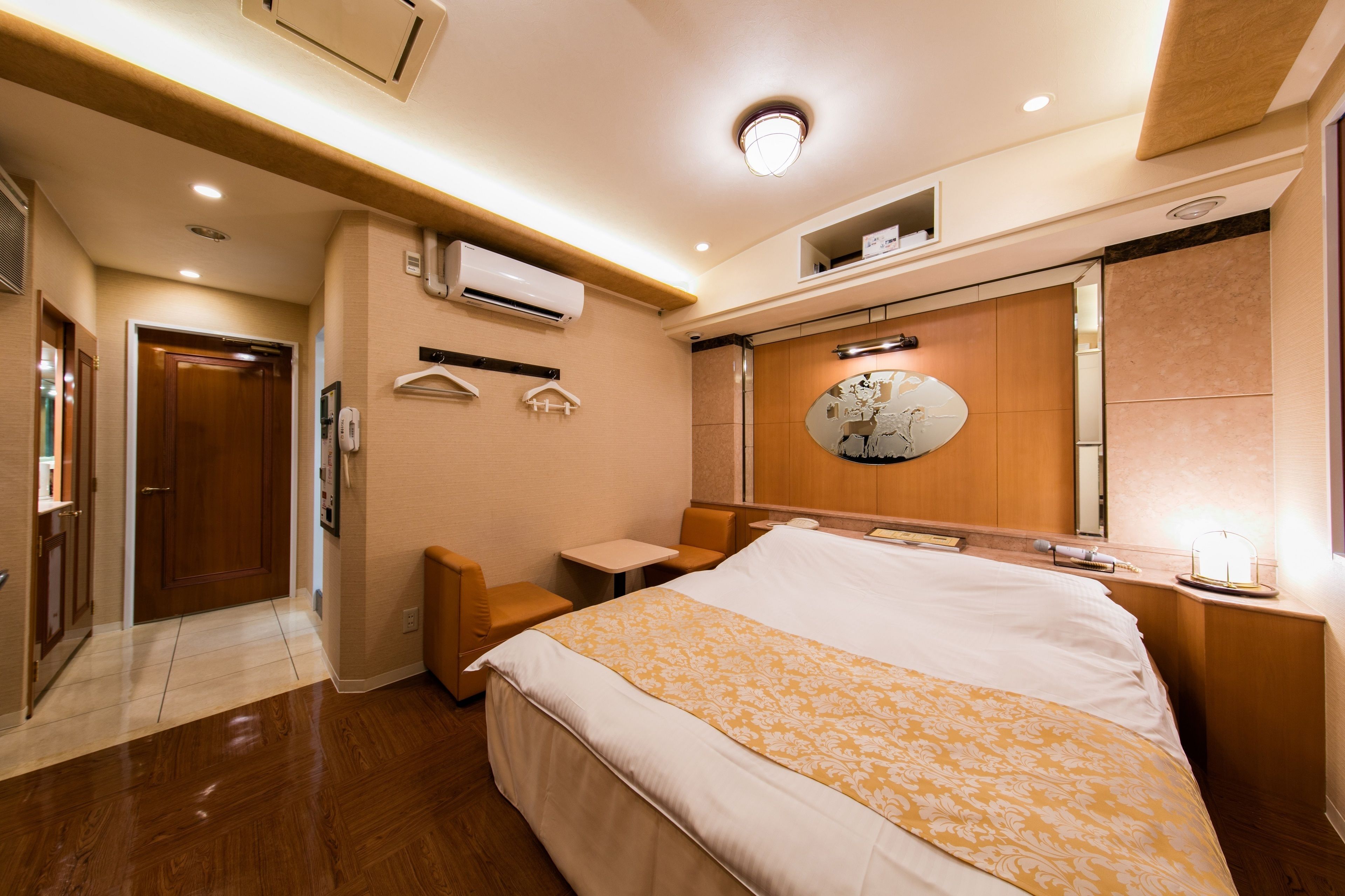 A hotel room with a large bed, a small table, a chair, a mirror, and an air conditioning unit.