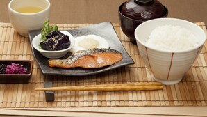 A traditional Japanese meal with salmon, rice, and a small bowl of pickled vegetables on a bamboo mat. - Fine Tsu (Tsu)