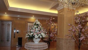 A lobby with a large floral arrangement on a round table, a chandelier, and a column with a tree. - Hotel Fine Garden Toyonaka Itami Airport (Toyonaka)