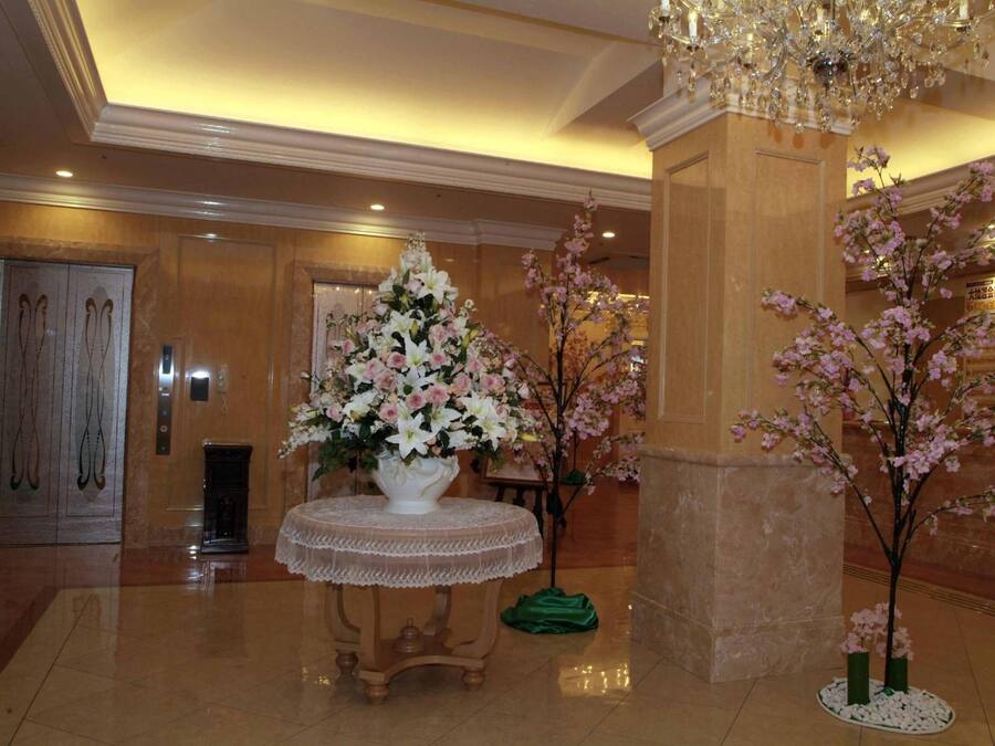 A lobby with a large floral arrangement on a round table, a chandelier, and a column with a tree.