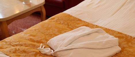 Una cama bien hecha con una toalla blanca doblada, una colcha amarilla y blanca estampada, y una silla de cuero rojo al fondo.