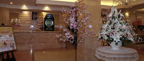 A lobby with a reception desk, a clock, a chandelier, and a floral arrangement on a table.