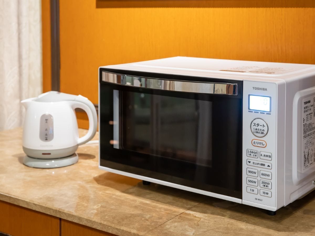 A Toshiba microwave oven with a digital display and control panel, placed on a kitchen countertop next to a white electric kettle.