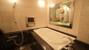 Un baño moderno con una bañera grande, un cabezal de ducha manual, un panel de control en la pared y un espejo con un adorno colgante decorativo.