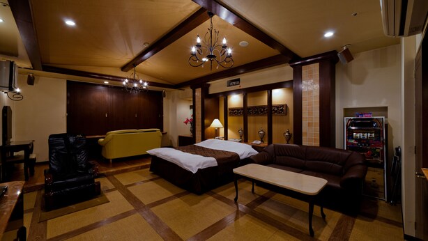 A hotel room with a bed, a sofa, a small table, a chair, a minibar, and a ceiling chandelier. - Hotel Fine Garden Toyonaka Itami Airport (Toyonaka)