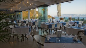 A restaurant with tables set for dining, large windows offering a view of the sea, and a chandelier hanging from the ceiling. - Sentido Bellazure (Bodrum)