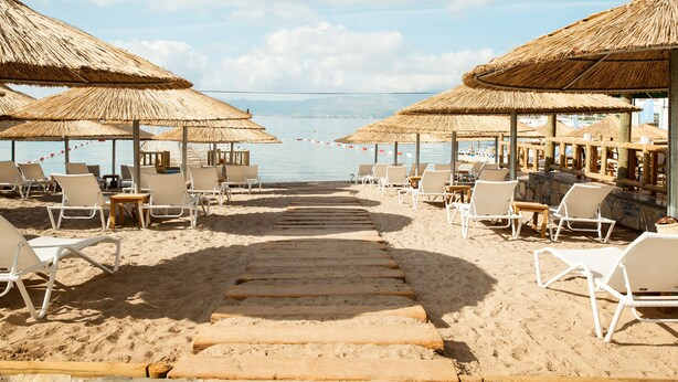 A beach with wooden walkways, white lounge chairs, and thatched umbrellas. - Sentido Bellazure (Bodrum)