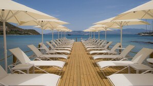 A wooden deck with rows of white lounge chairs and umbrellas, leading to a body of water with mountains in the background. - Sentido Bellazure (Bodrum)