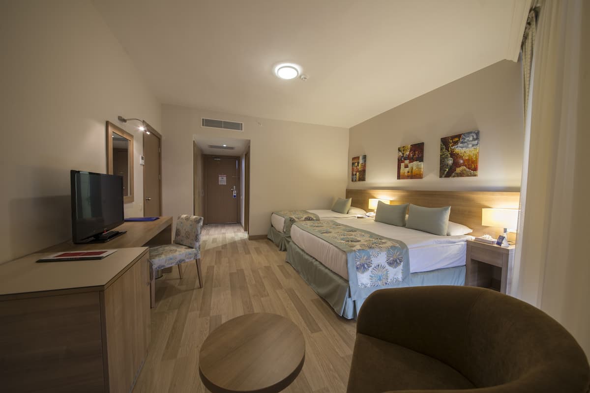 A hotel room with a bed, two bedside tables, a desk with a TV, a chair, and a round table.