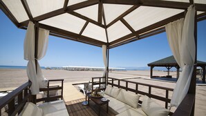 A covered outdoor seating area with a wooden deck, white cushions, and a table with a bowl of fruit.