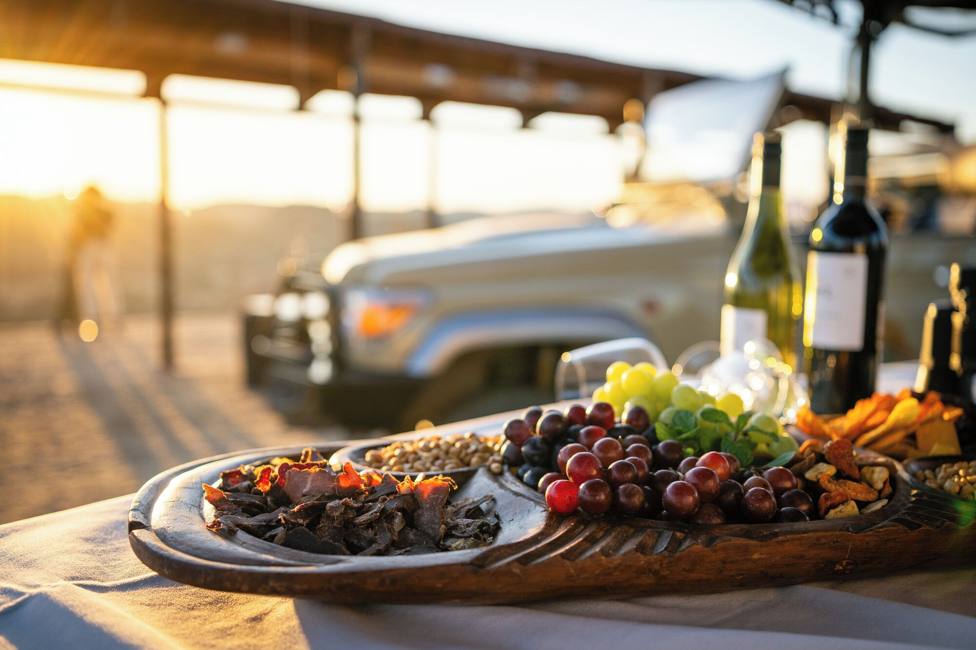 A wooden board with various foods and a bottle of wine on a table outdoors.