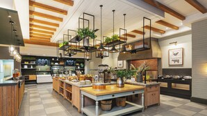 Una cocina moderna con una isla central, vigas de madera en el techo, lámparas colgantes y una variedad de plantas y utensilios de cocina.