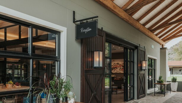 A reception area with a wooden bench, potted plants, and a sign above the entrance. - Midgard (Okahandja)