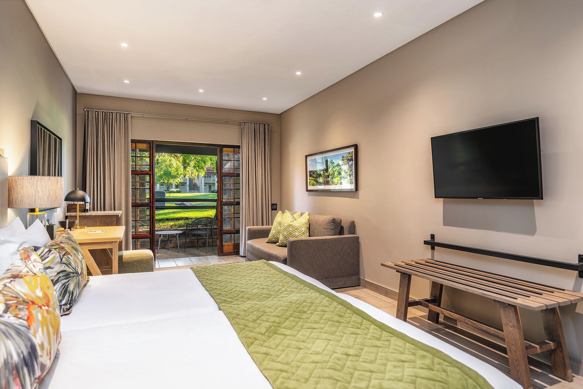 Habitación de hotel con cama, televisor, escritorio y vistas a un jardín.