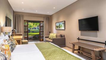 Habitación de hotel con cama, televisor, escritorio y vistas a un jardín.