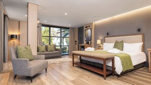 A modern hotel room with a large bed, a sofa, a chair, and a dining table. - Midgard (Okahandja)
