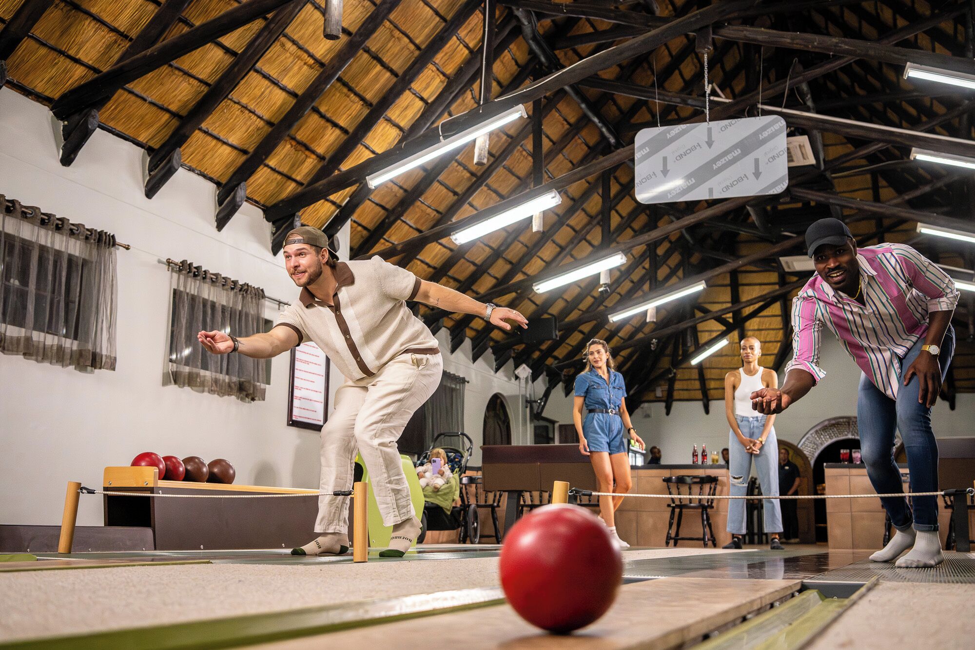 Een bowlinghal met houten balken, een rode bowlingbal en mensen die bowlen.