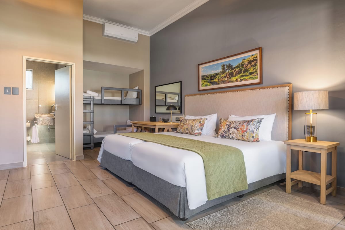Un cuarto de hotel con una cama grande, una mesita de noche, una lámpara, un cuadro en la pared y un baño visible a través de una puerta abierta.