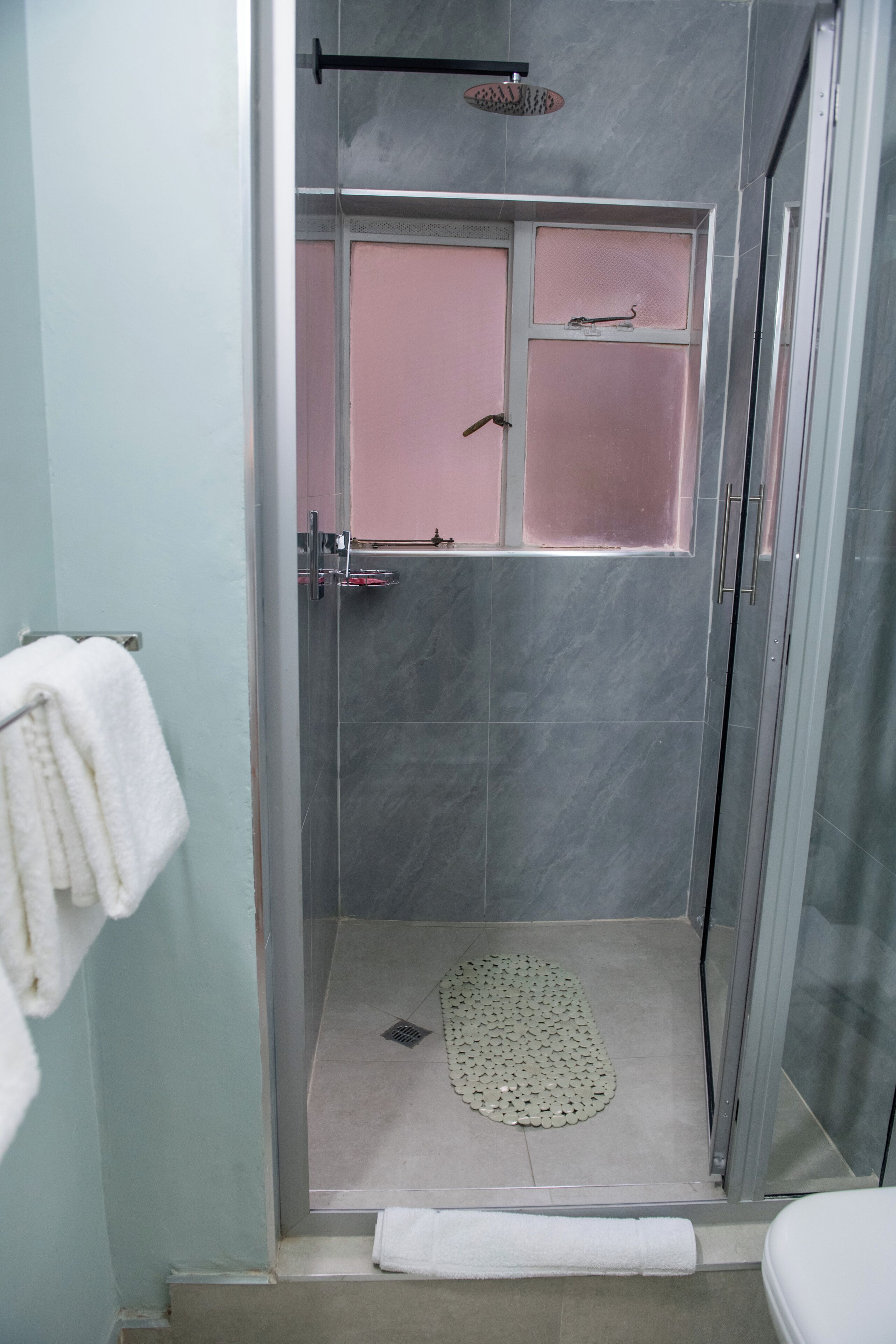 Una ducha a nivel con puerta de vidrio, un perchero y un cabezal de ducha.