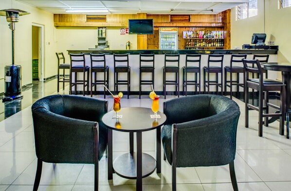 A bar area with multiple seating options, a television mounted on the wall, and a bar counter with various bottles and a cash register. - New Ambassador Hotel (Harare)