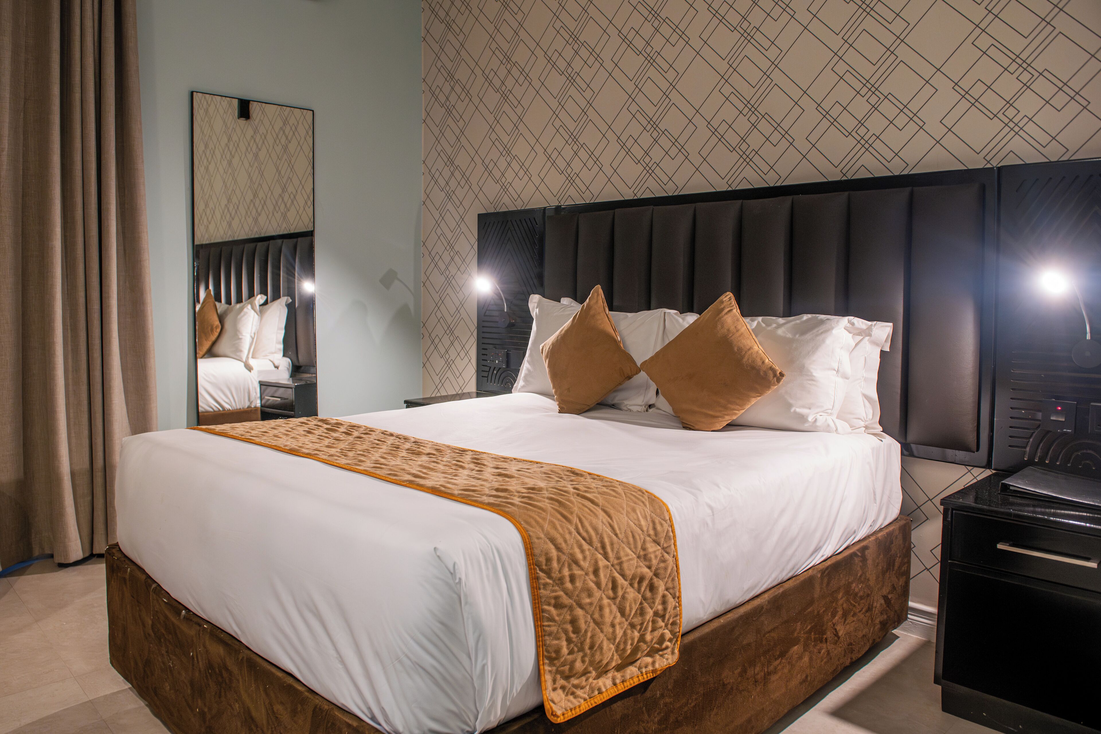 A neatly made bed with a quilted blanket, a headboard with a geometric pattern, and a mirror above it.