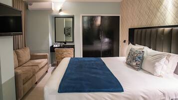 Habitación de hotel con cama, sofá, televisión, aire acondicionado, espejo y puerta.