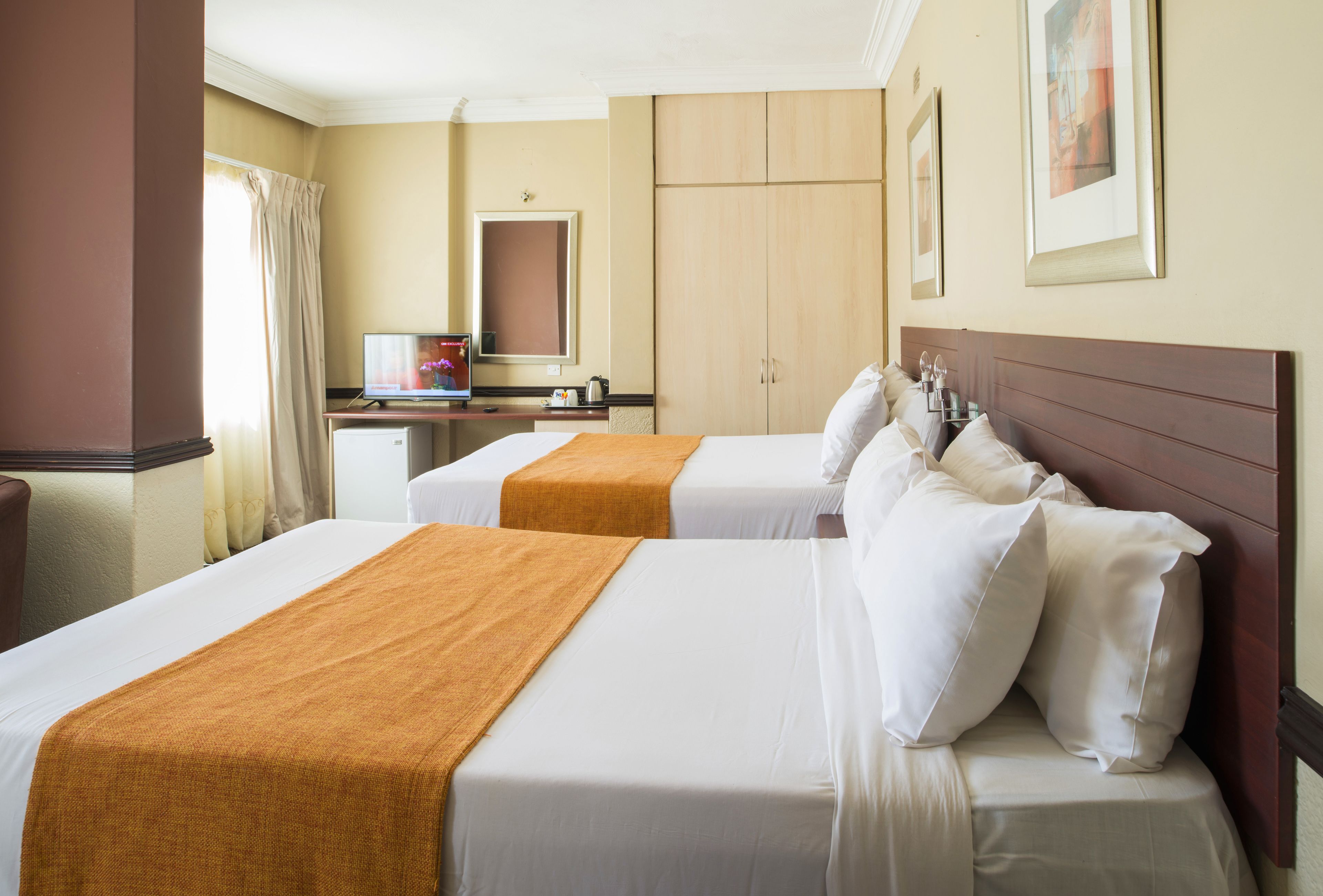 Una habitación de hotel con dos camas, un escritorio con computadora, un espejo y un armario.