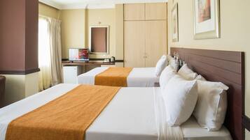 Una habitación de hotel con dos camas, un escritorio con computadora, un espejo y un armario.
