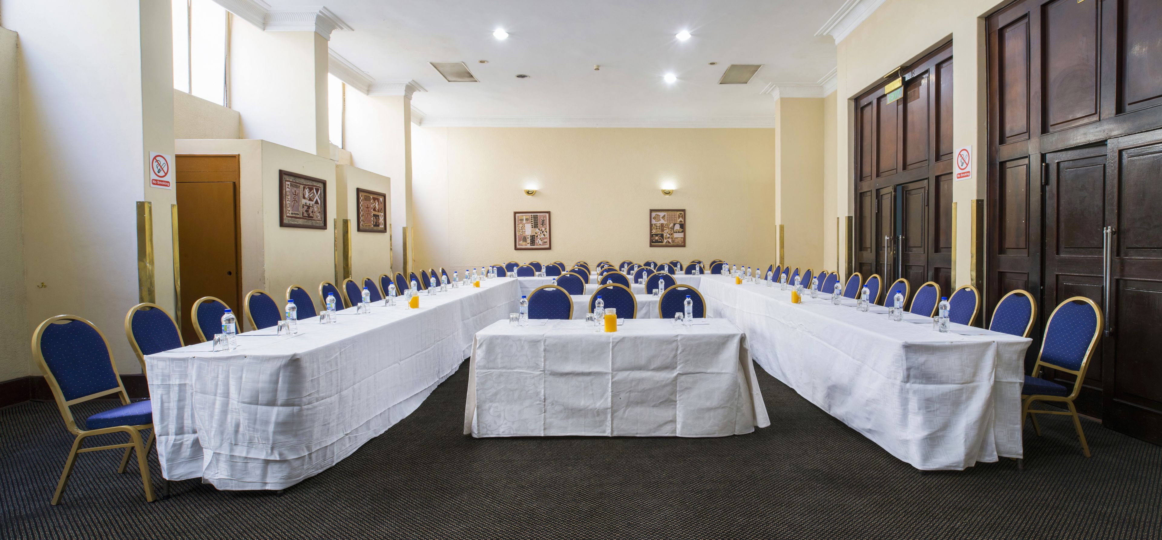 A conference room with long tables, blue chairs, and white tablecloths.