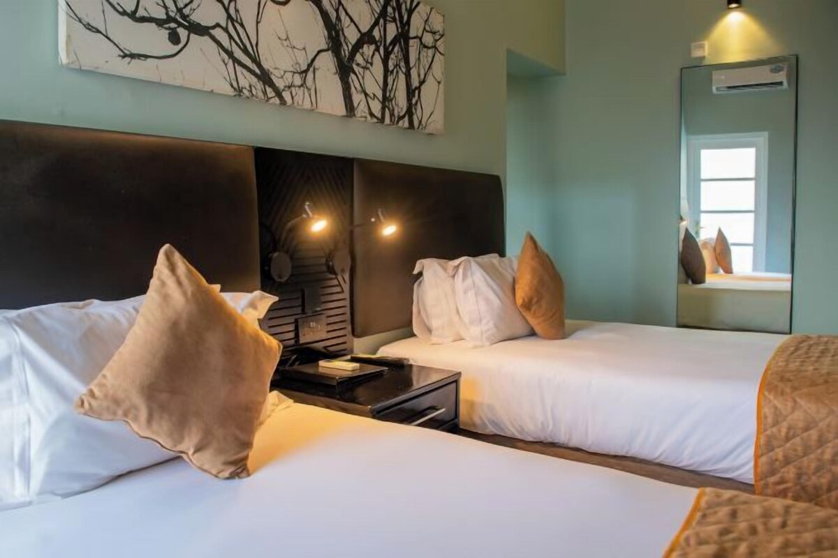 Una habitación de hotel con dos camas, una mesita de noche, una obra de arte colgada en la pared y una ventana con vistas.