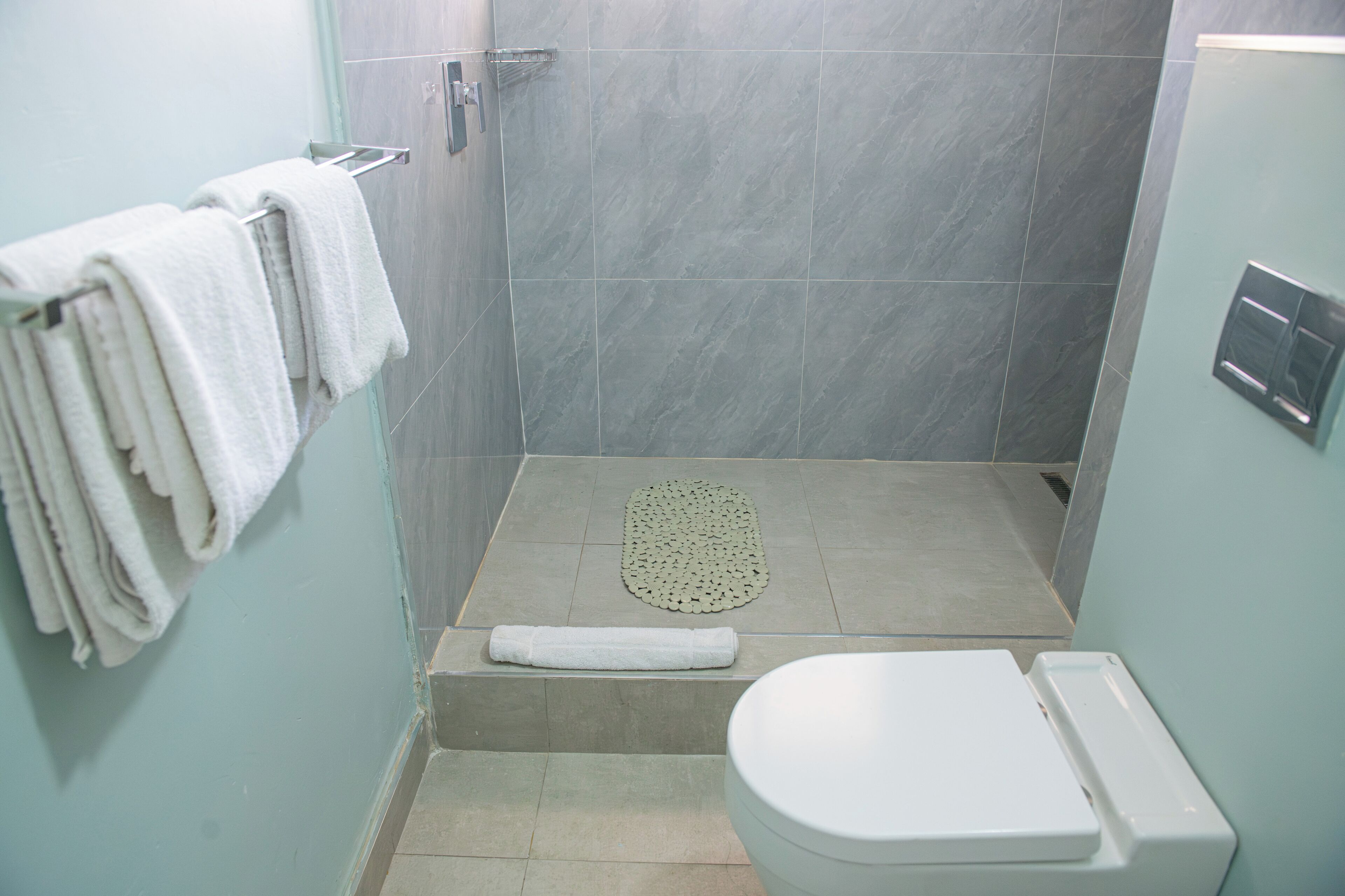 A bathroom with a shower, a toilet, and a towel rack with towels.