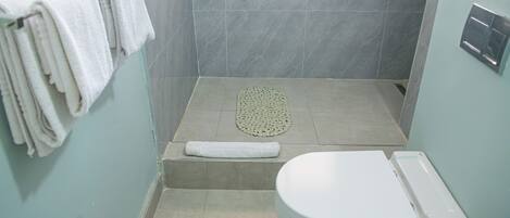 A bathroom with a shower, a toilet, and a towel rack with towels.