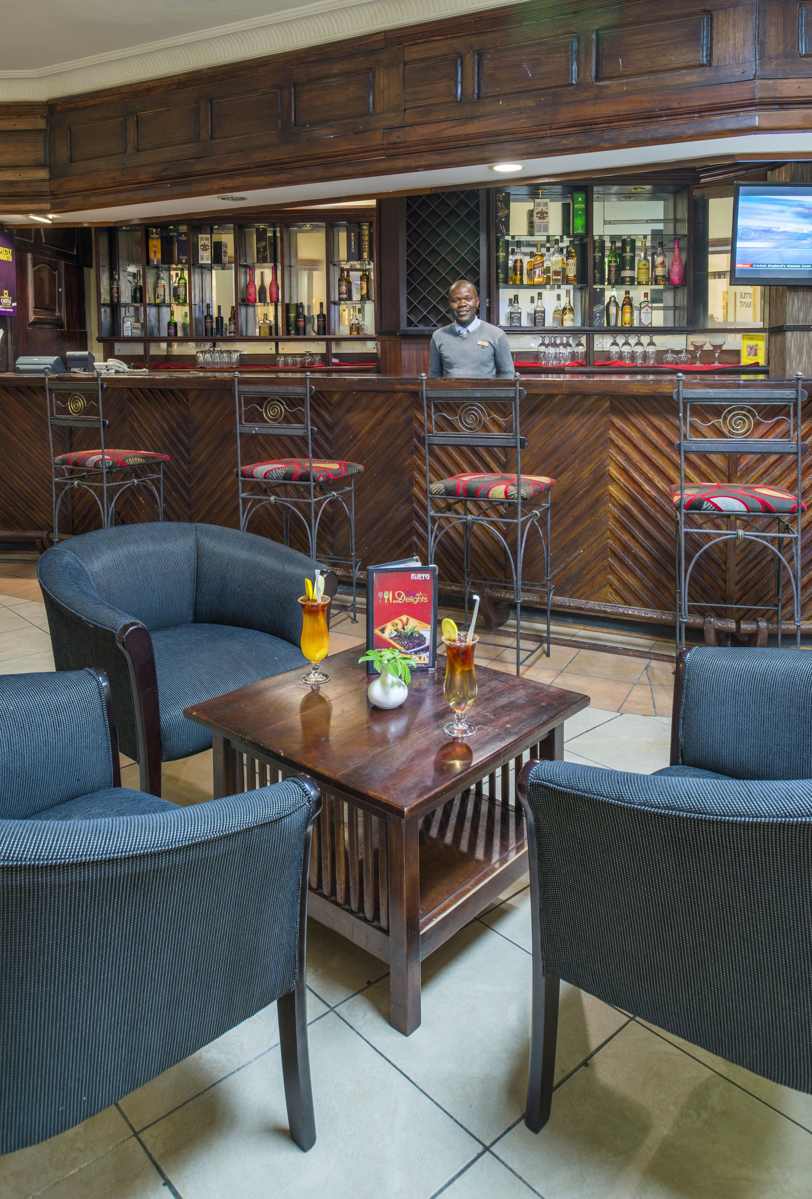 A bar area with wooden paneling, a bartender, and bar stools.