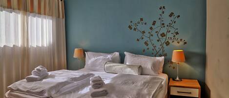 A neatly made bed with towels, a nightstand with a lamp, and a wall with a floral design.