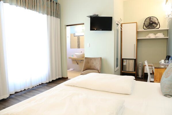 A hotel room with a bed, a TV mounted on the wall, a fan, and a bathroom visible through an open door. - Namib Guesthouse (Swakopmund)