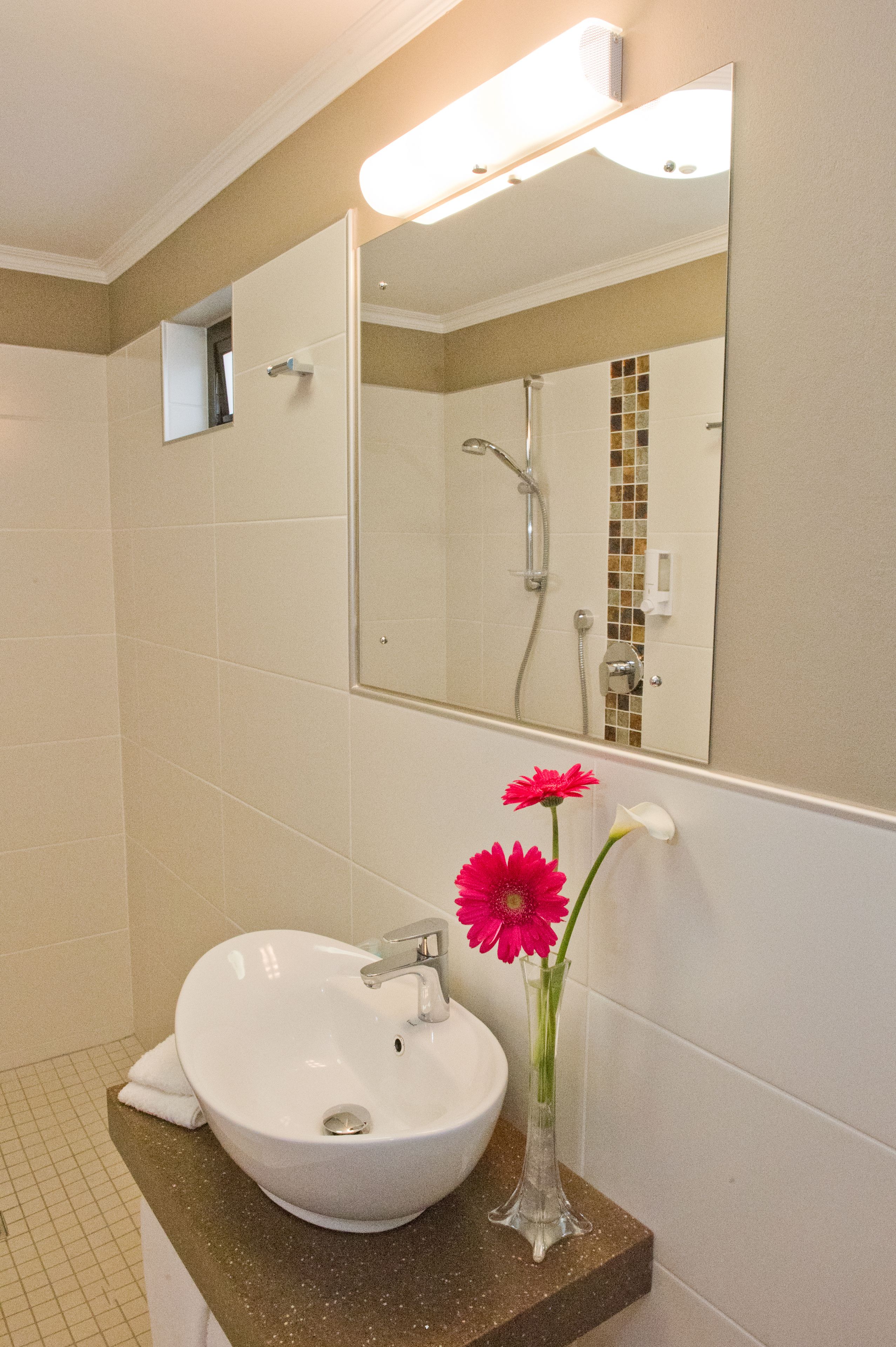 A bathroom with a white sink, a mirror, and a vase with flowers.