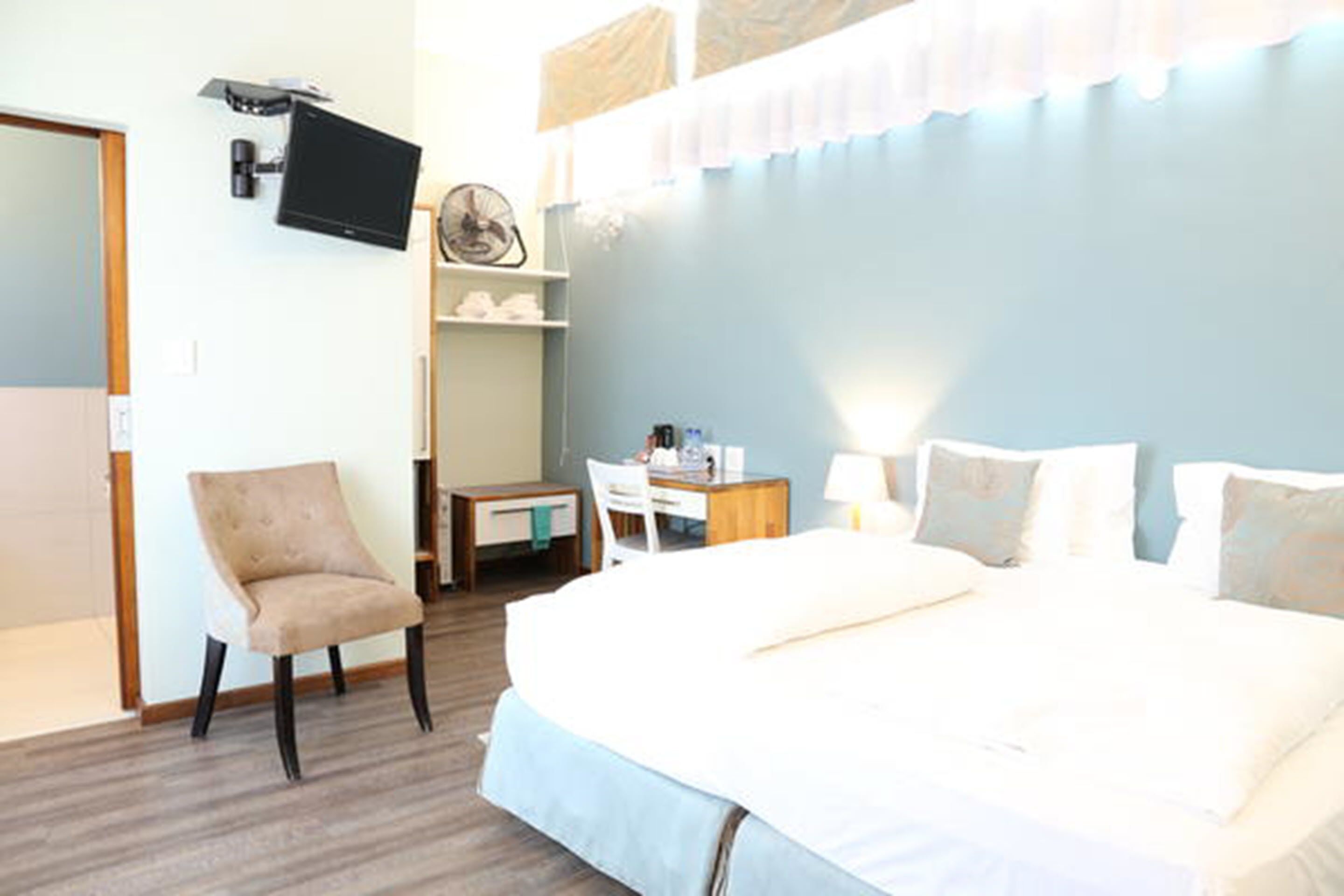 Ett hotellrum med en säng, ett skrivbord, en stol, en tv och en fläkt.
