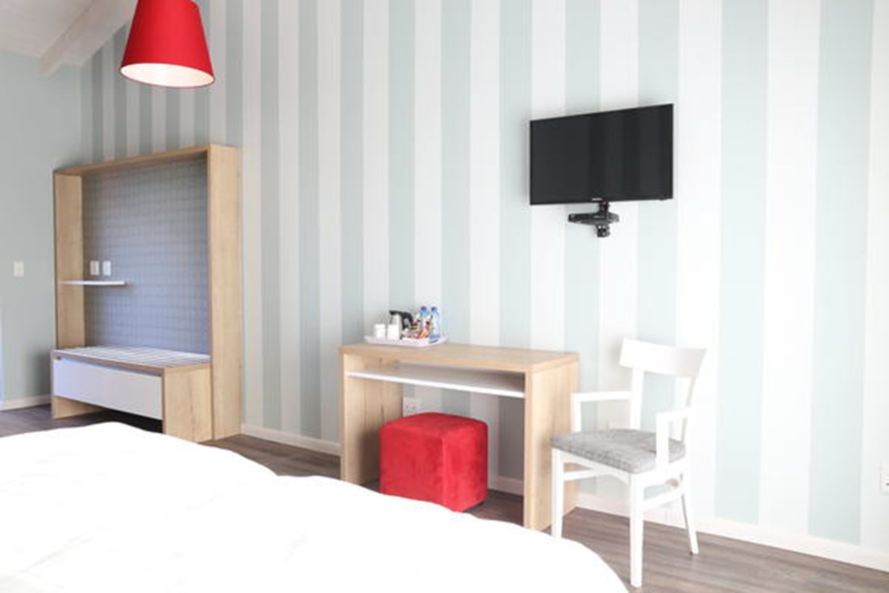 Een slaapkamer met een bed, een bureau, een stoel, een televisie en een rode lamp.