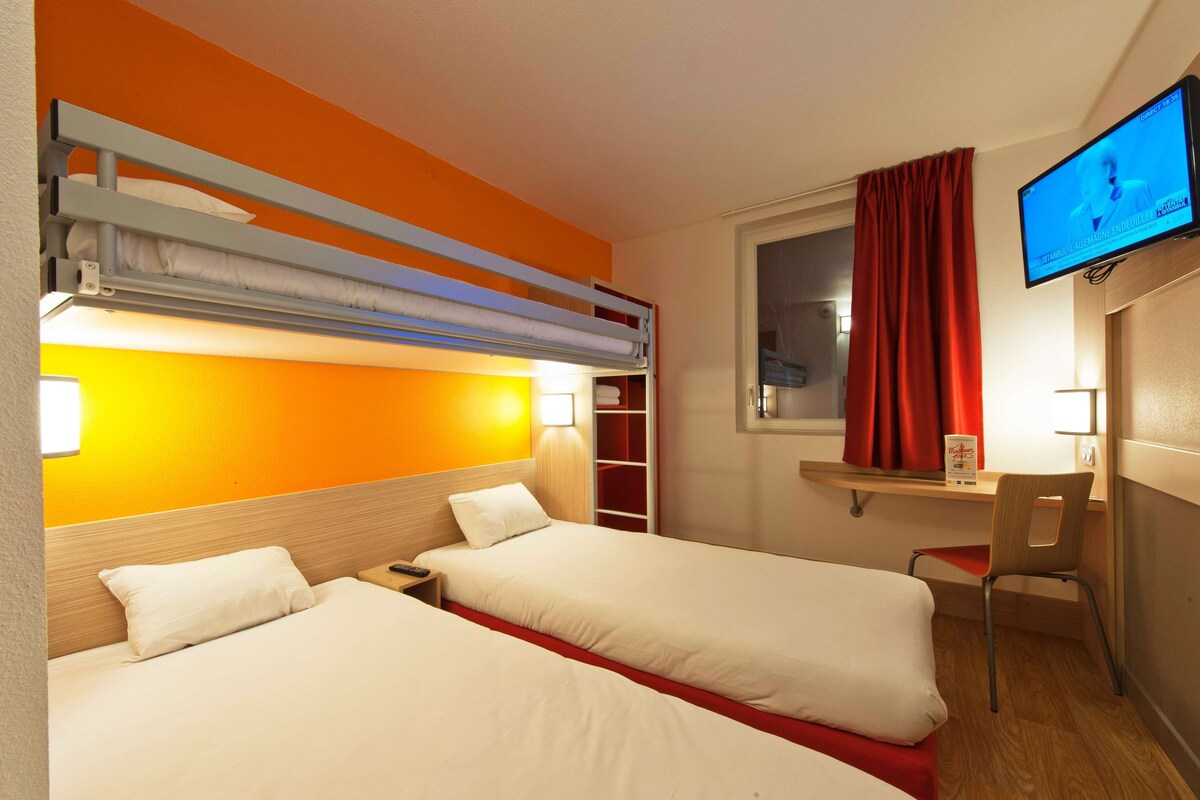 A hotel room with two beds, a desk, a chair, a TV, and a window with curtains.
