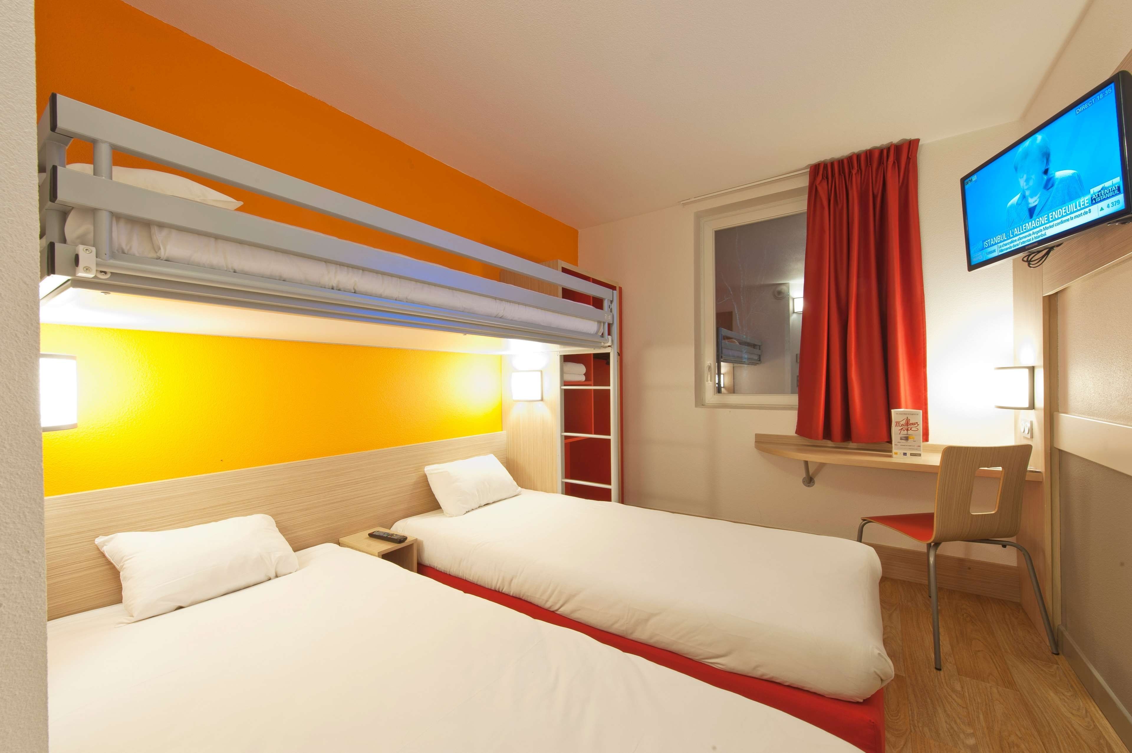 A hotel room with two beds, a desk, a television, and a window with curtains.