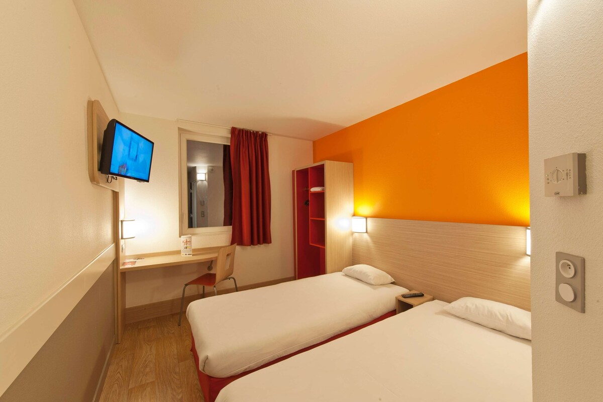 A hotel room with two beds, a desk, a chair, a television, and a red curtain.