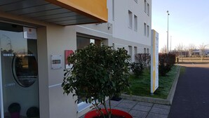 Entrada de hotel con una planta en maceta roja, puerta de vidrio y un letrero que dice 'Louvre Hotels'.