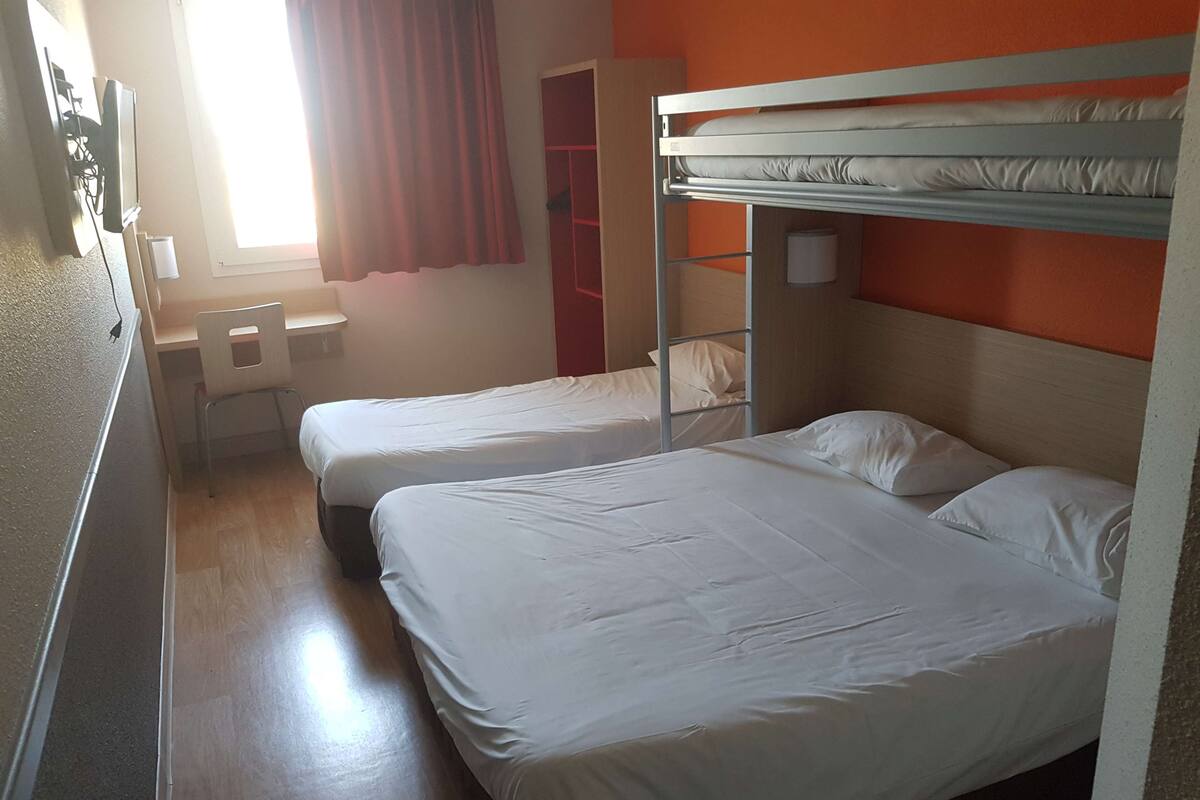 A dormitory room with bunk beds, a desk, and a chair.